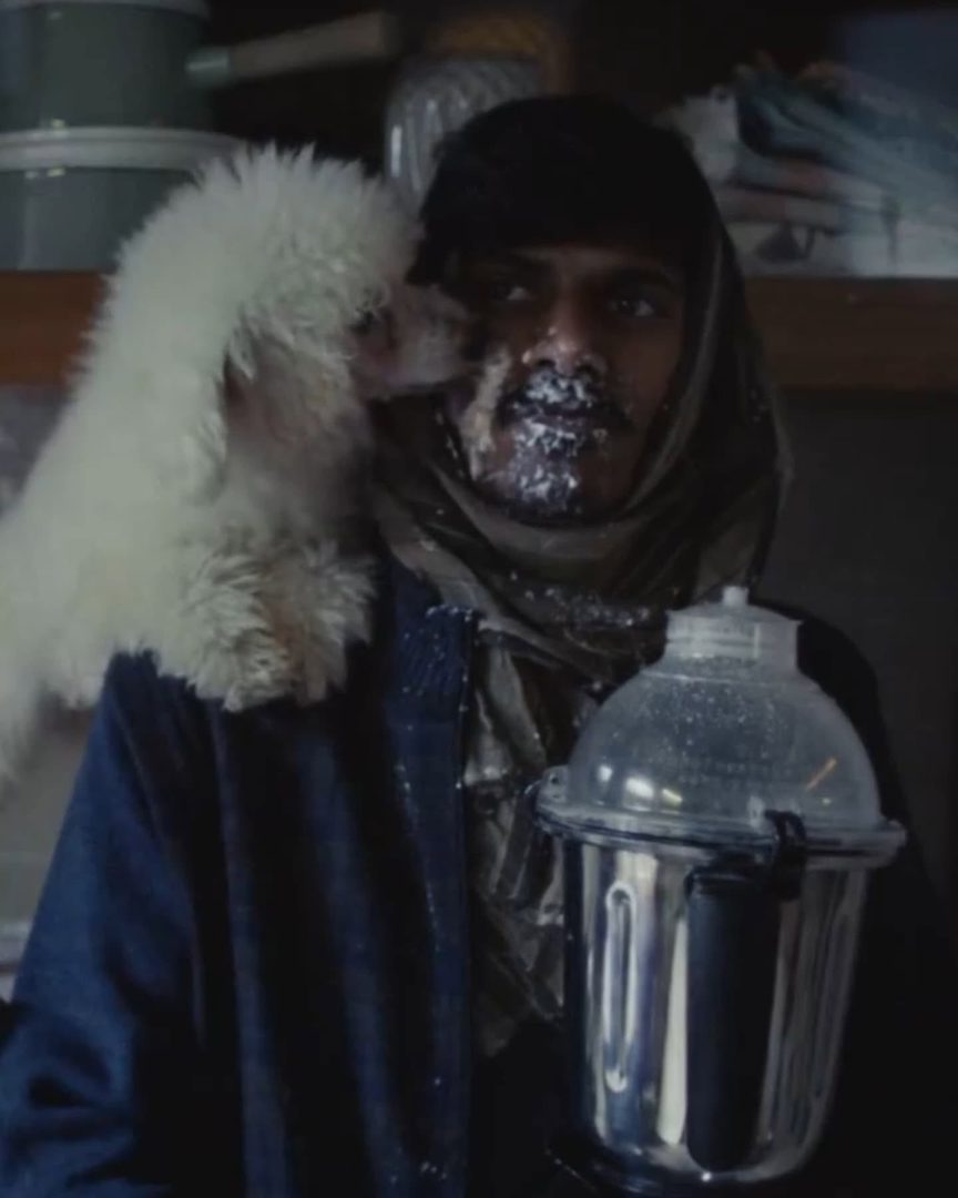 J D Ayush Kumar in the Swiggy Instamart commercial - face flecked white, a small white dog on his shoulder, holding a mixer jar